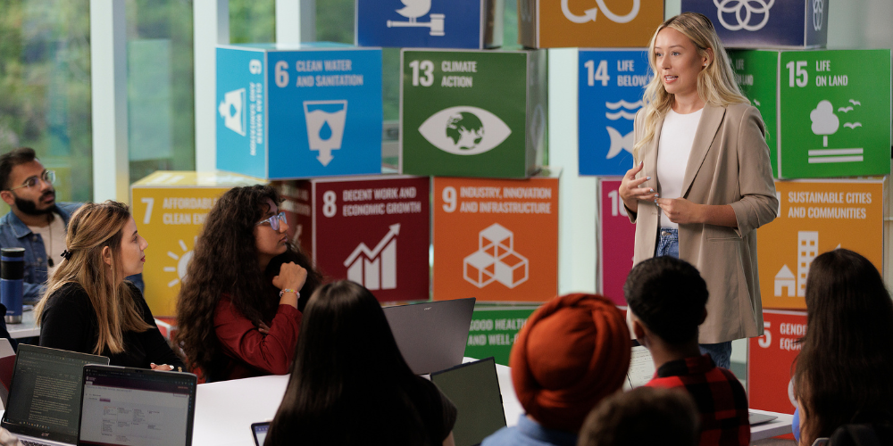 Adrianna presents in front of colourful blocks which outline the SDG