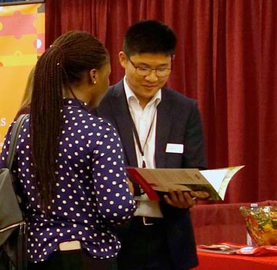 A Saint Mary's university student with their back to the camera speaking with a career fair advisor who is facing the camera while showing a brochure.