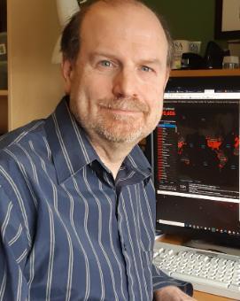 Dave, a white man with facial hair, sits at a desk with a computer screen in the background