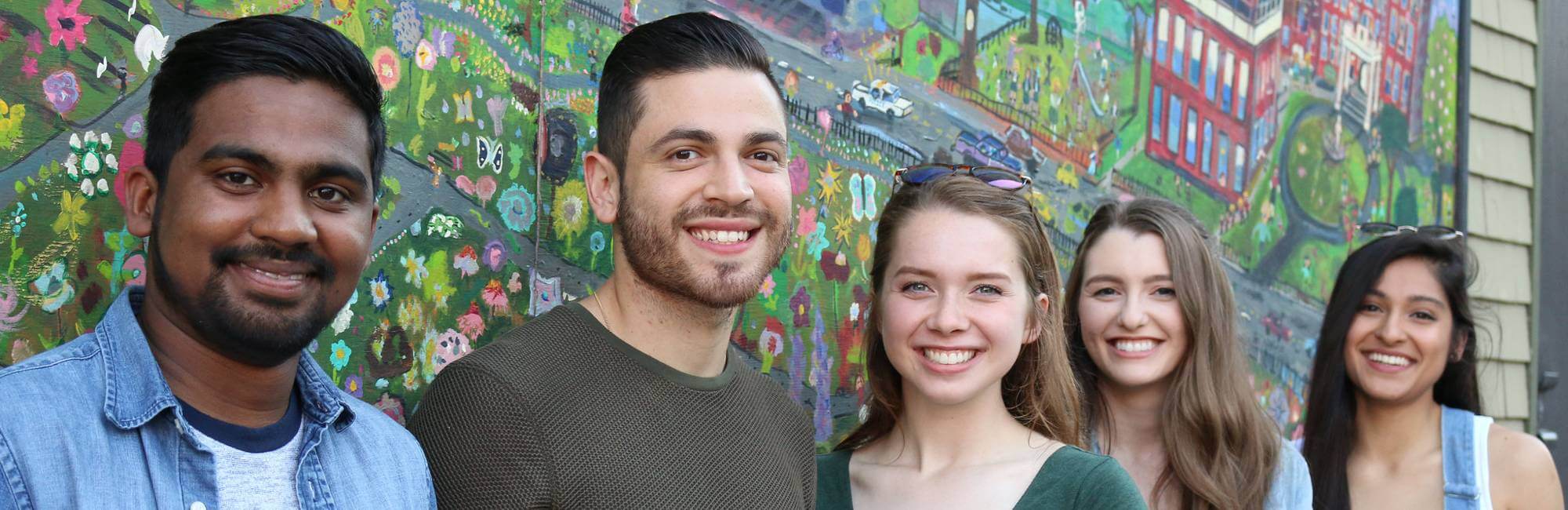 Smiling students line up against a wall with graffiti.