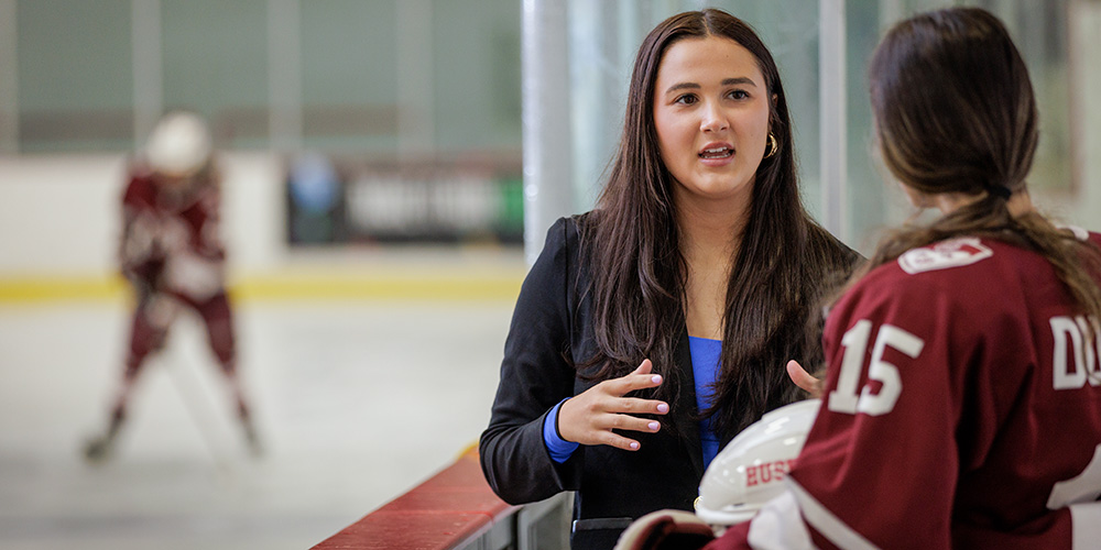 A hockey coach is talking to a player beside the rink.