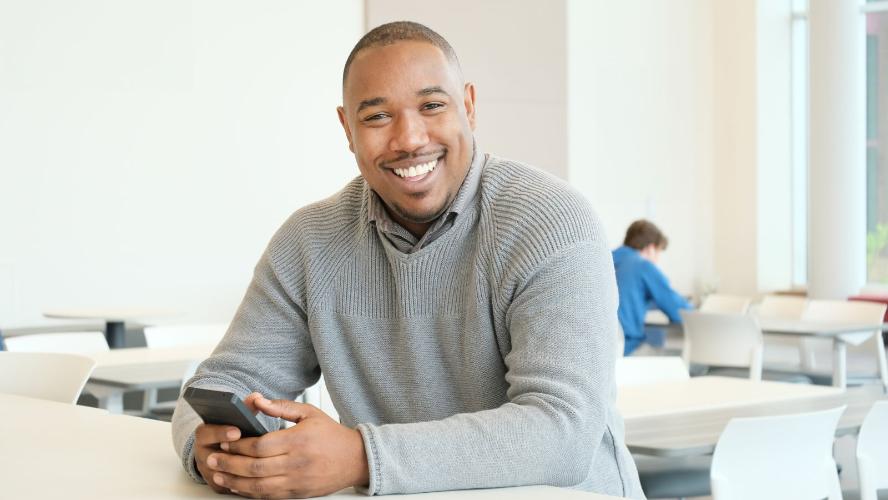 Odane Finnegan leaning on a white table, holding a phone and smiling at the camera