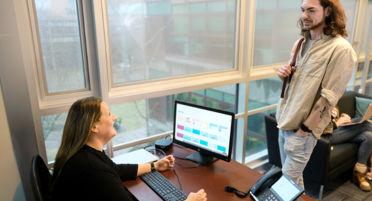 Student standing in front of person at desk both smiling