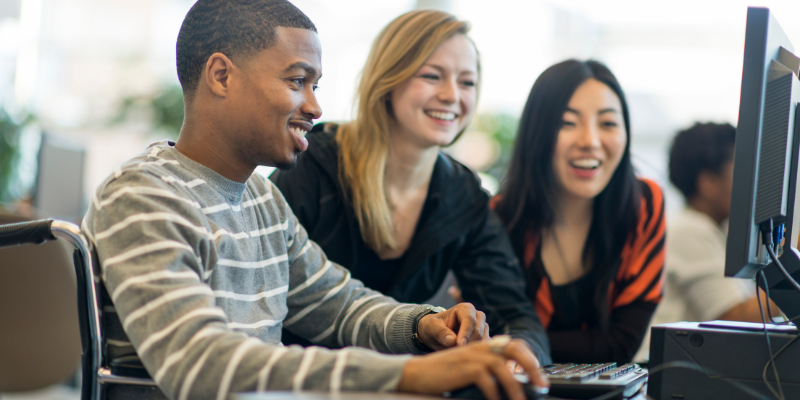 3 students, 1 in a wheelchair, sitting together looking at a computer