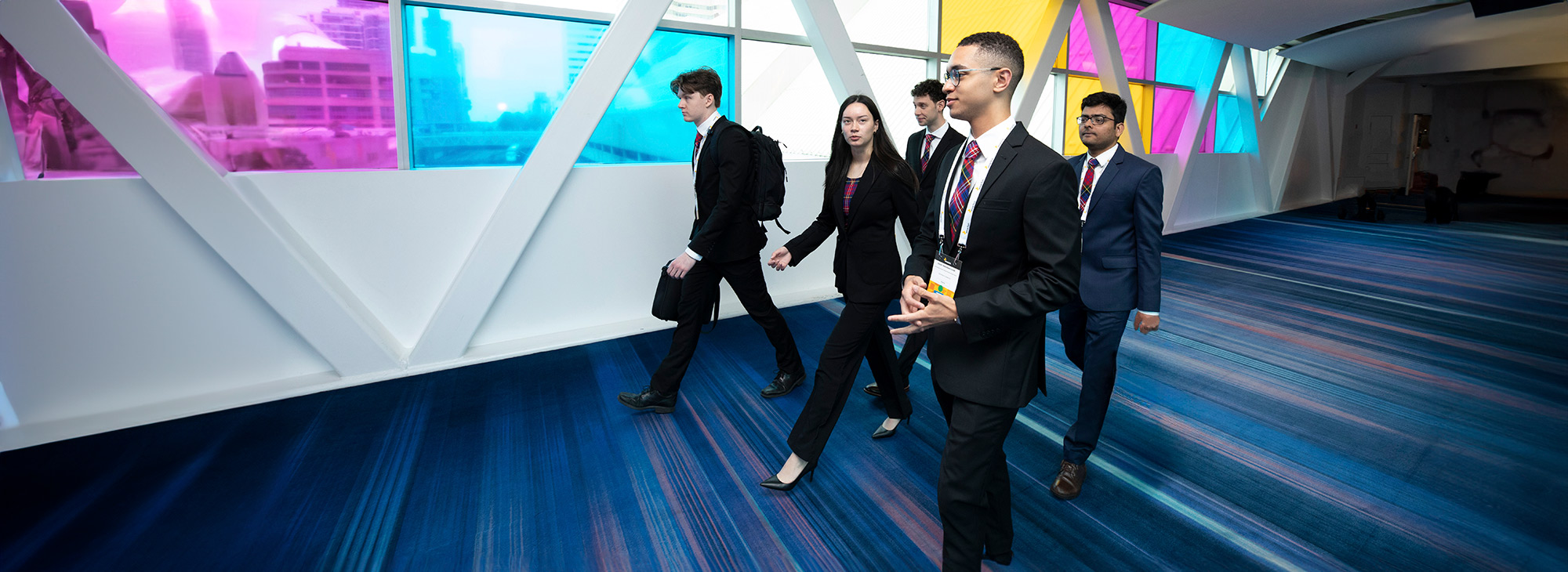 A group of students in business clothes waling purposefully down a hallway.